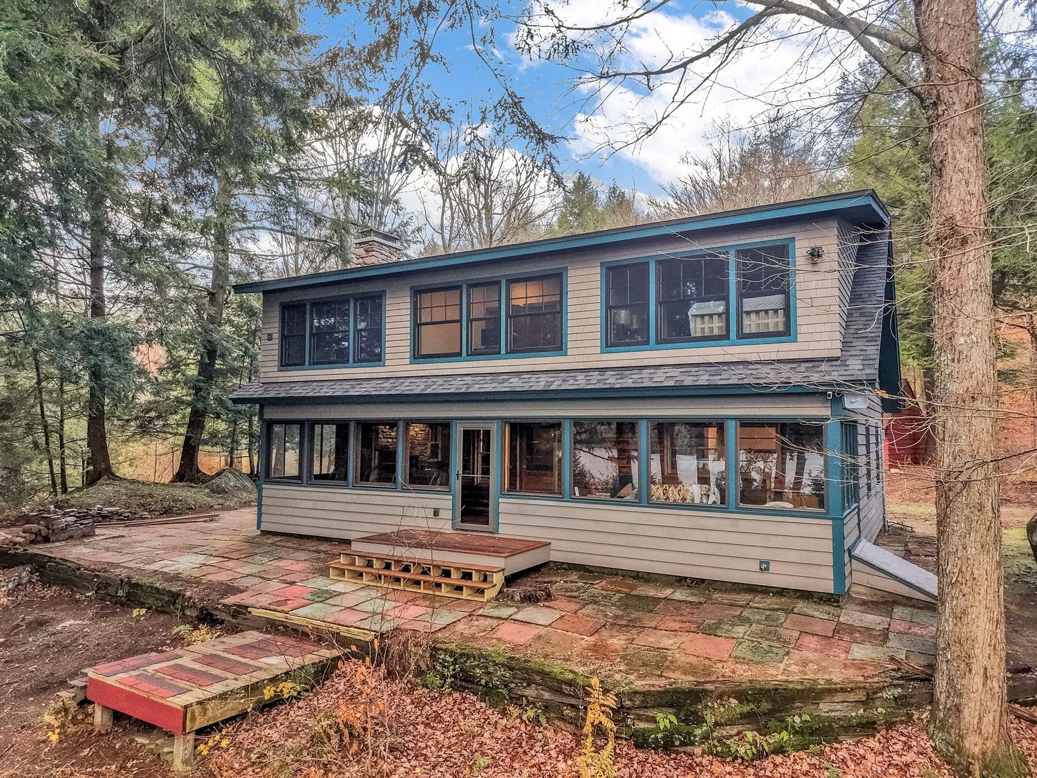 Long mid-century modern ranch home with blue trim and large windows nestled among autumn trees in wooded setting.