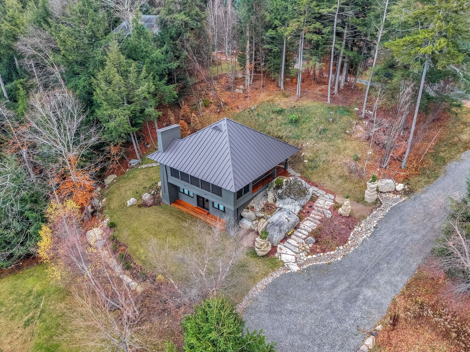 Modern gray-roofed gazebo surrounded by landscaped gardens and fall foliage in a wooded setting.