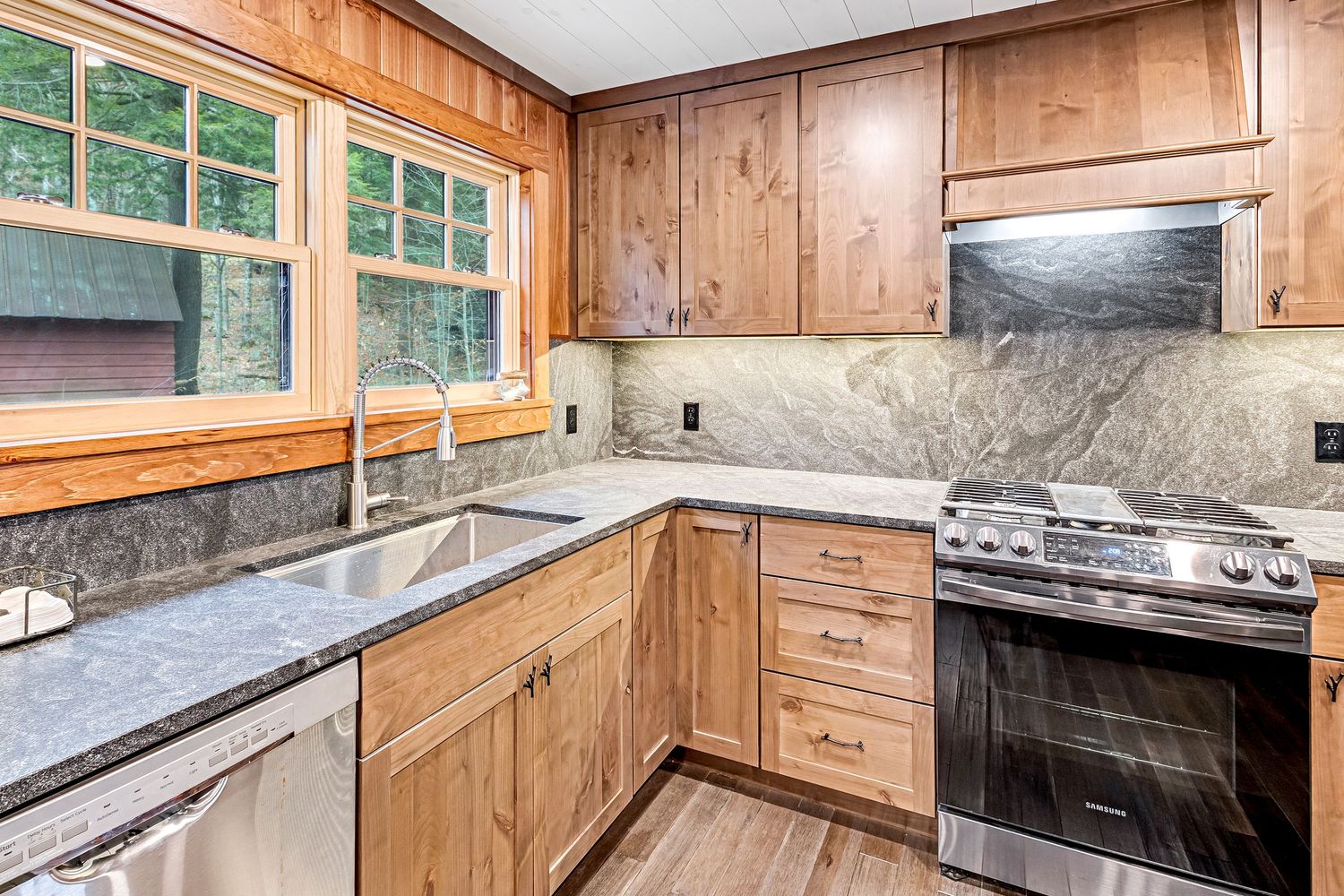 Contemporary kitchen featuring natural wood cabinets, granite countertops, and stainless steel appliances with window views.