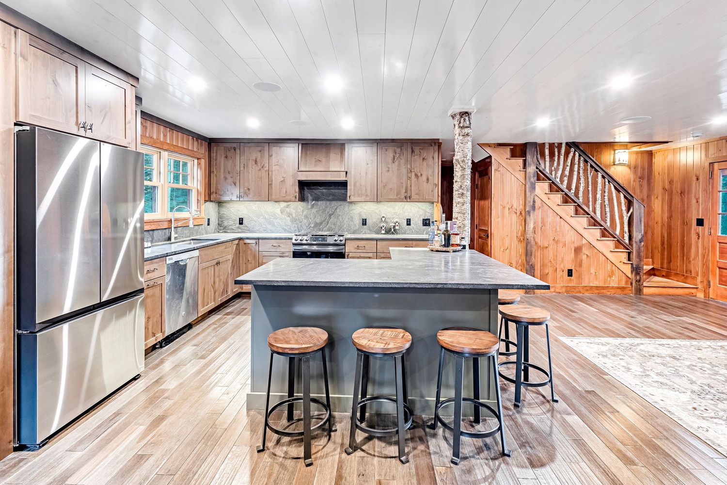 Modern rustic interior panorama showing open concept living space with wood floors and white ceiling beams.