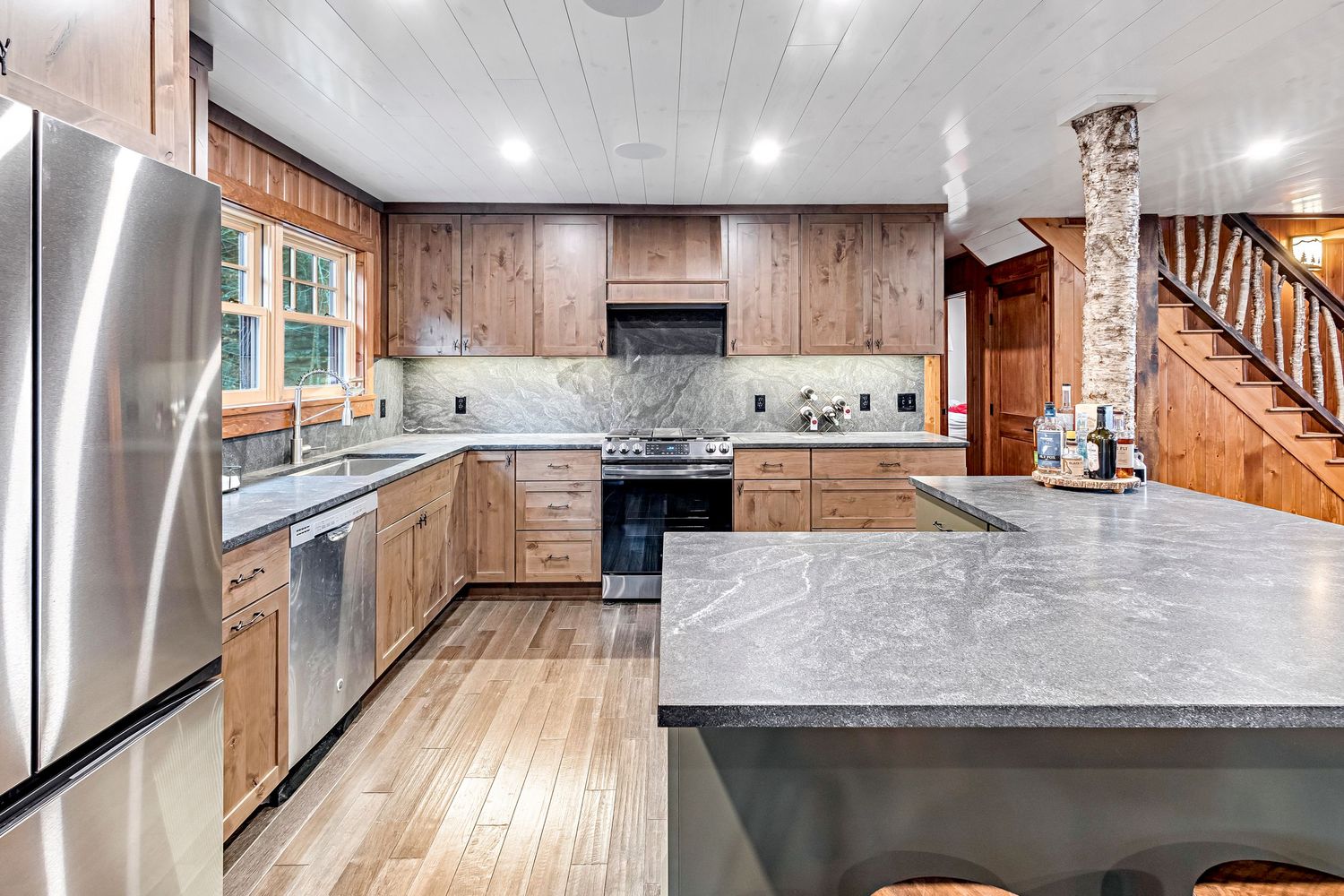 Modern kitchen interior with wood paneled walls, grey quartz countertops, and stainless steel appliances.