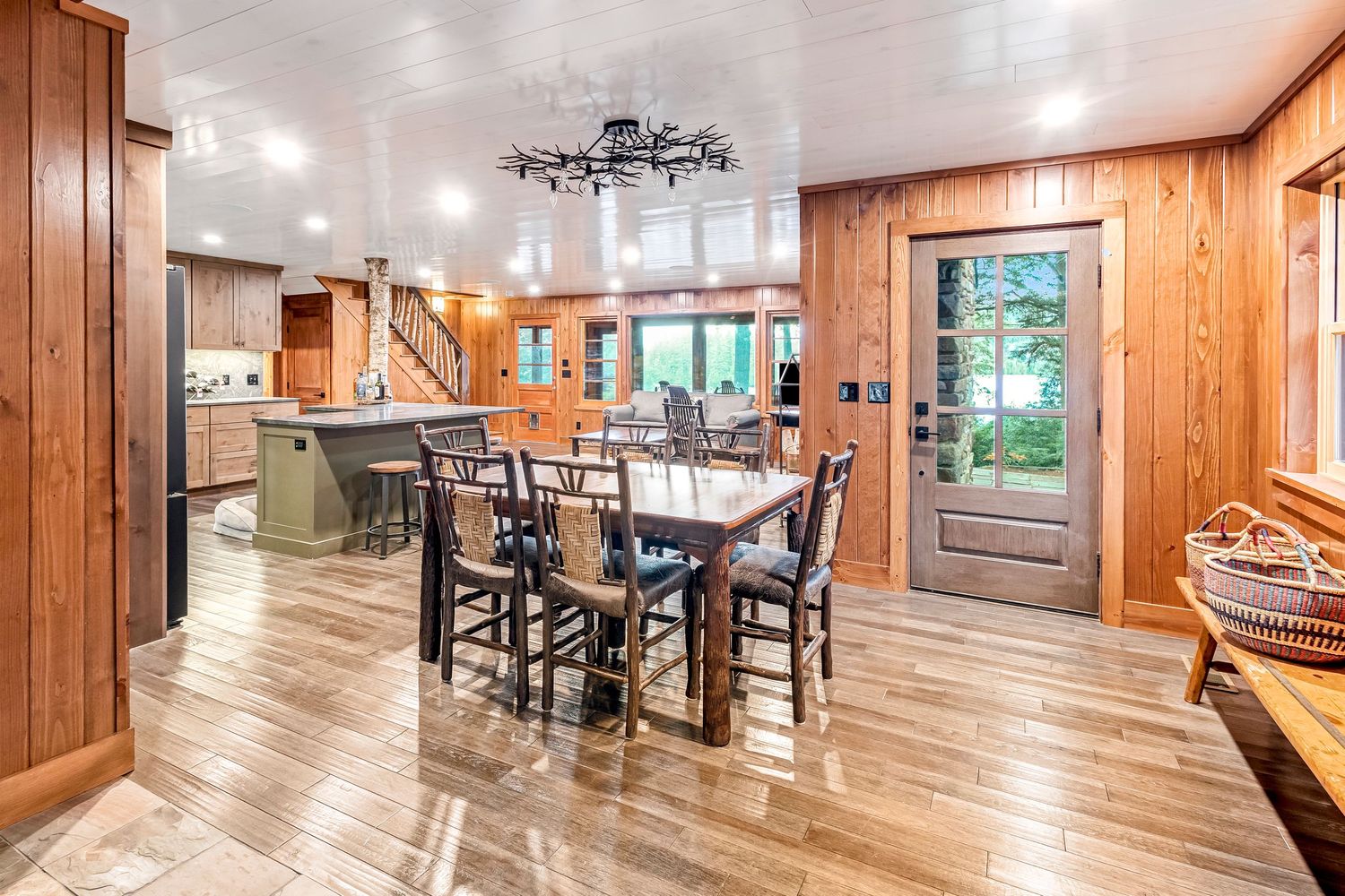 Rustic dining area with wooden walls, hardwood floors and large table beneath chandelier.