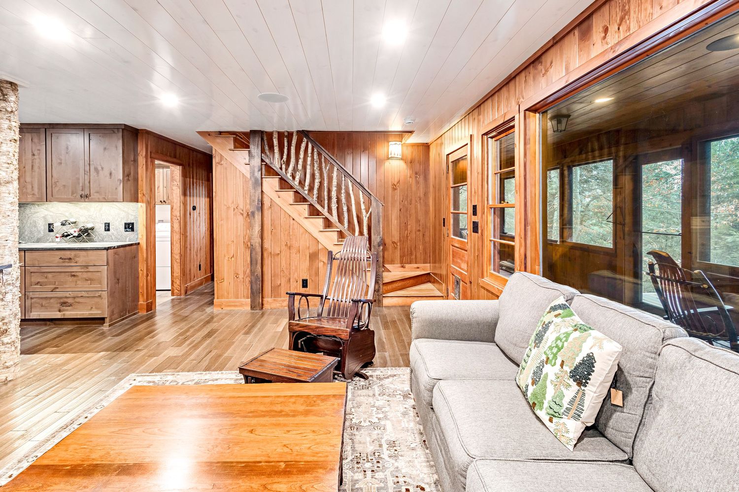 Rustic open concept living area with wood paneled walls, hardwood floors, and modern recessed lighting.
