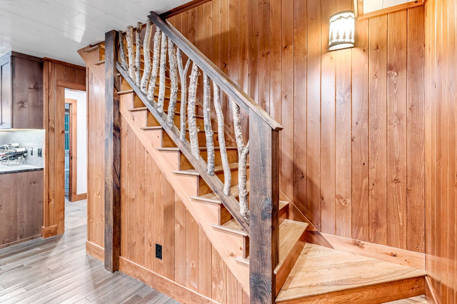 Rustic wood-paneled staircase with white birch tree trunks used as decorative railing posts in a cabin interior.
