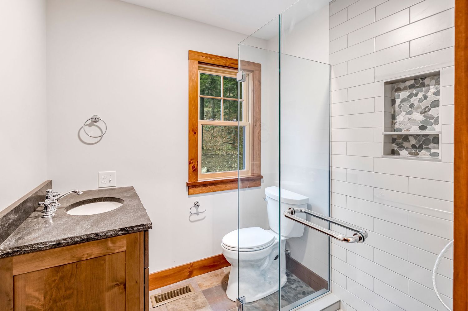 Modern bathroom featuring white subway tile walls, glass shower enclosure, and wooden framed window.