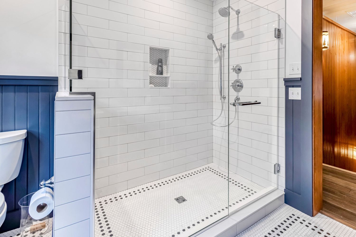 Modern white subway-tiled bathroom with glass shower enclosure and navy blue accents.