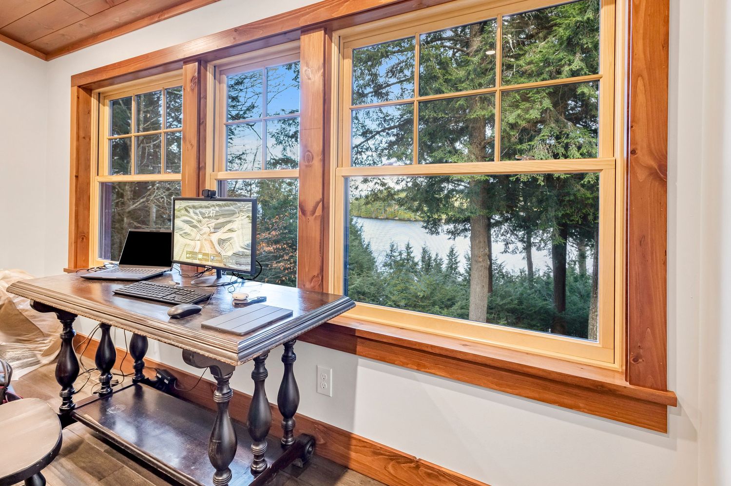 Home office desk facing large windows with panoramic lake and forest views.
