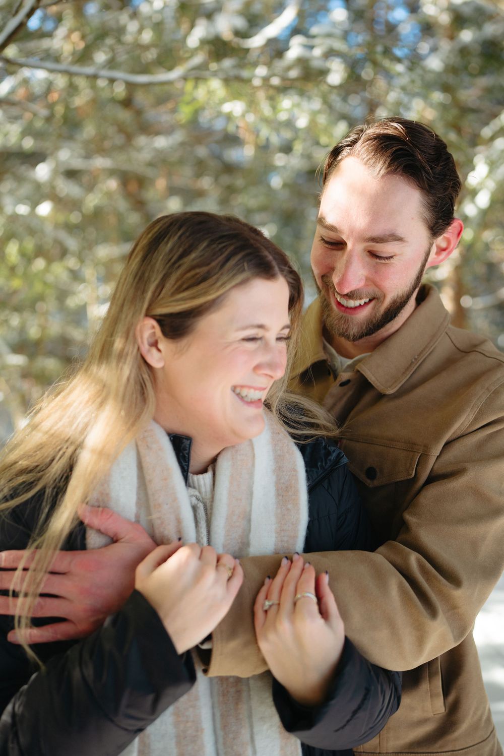 A romantic couple shares joyful laughter while embracing outdoors in winter clothing.