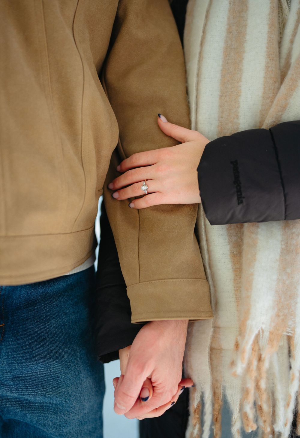 Close-up view of two people holding hands while wearing beige and dark colored clothing.