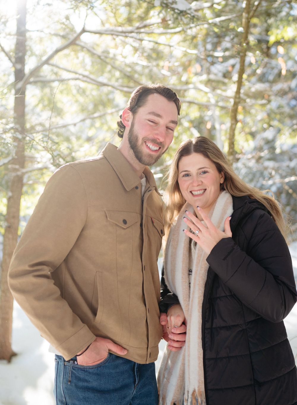 A couple shares joyful laughter while embracing in a snowy winter forest setting.