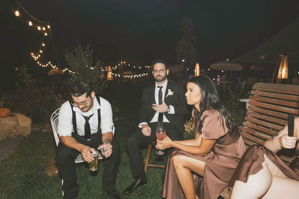 Wedding party dances and mingles under romantic outdoor lighting at an evening reception.