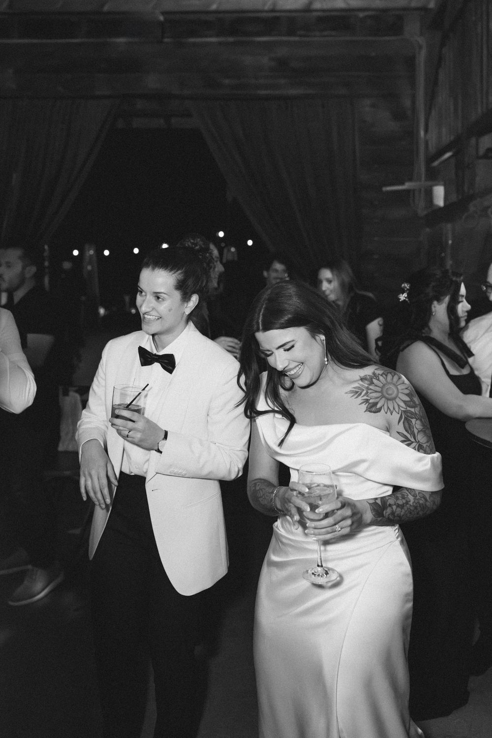 Couples slow dance together in elegant formal attire at dimly lit wedding reception.