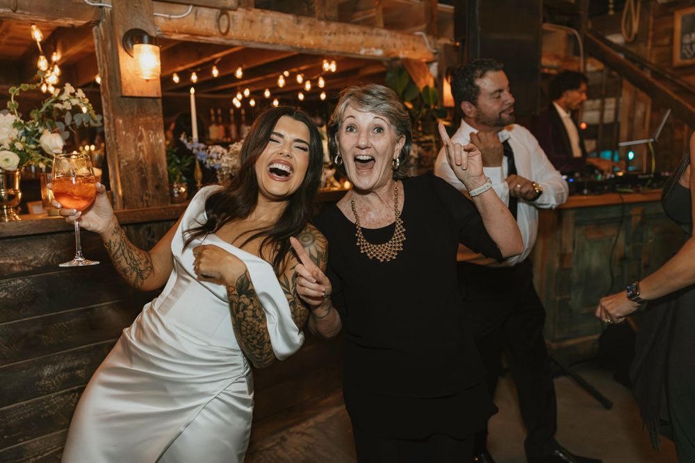 Lively wedding reception dancing with guests celebrating under rustic wooden beams and string lights.