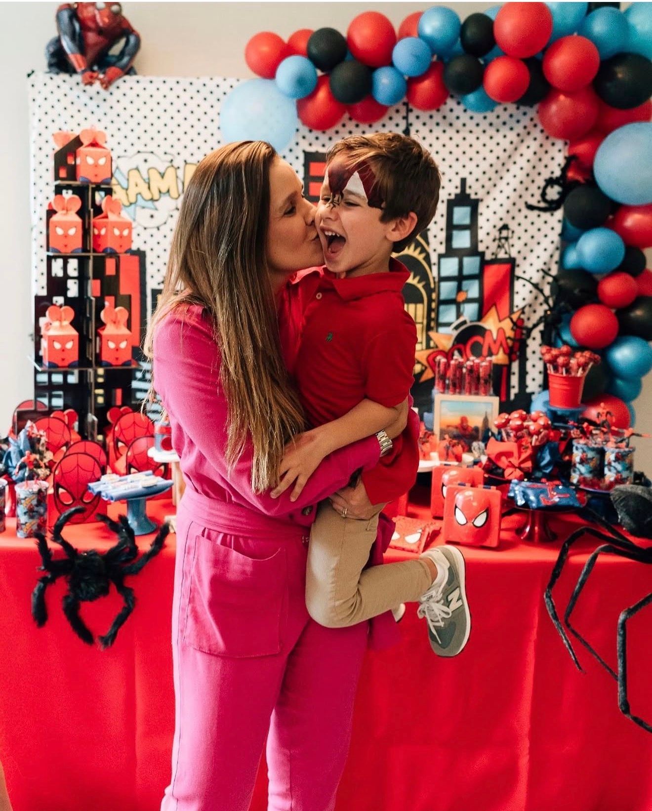 A festive Spider-Man themed party setup with red and blue balloon arch and decorative cityscape backdrop.