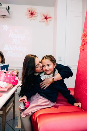 A sweet moment captured in a photo booth with red seating and pink floral decorations.