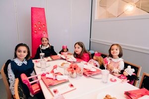 People sitting at decorated tables with pink and red Valentine's Day themed party decorations and treats.