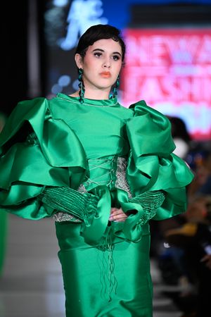 Model showcases vibrant emerald green ruffled gown with dramatic sculptural details on fashion runway.
