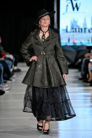 Model walks runway in olive green textured coat with black tulle skirt during fashion show.