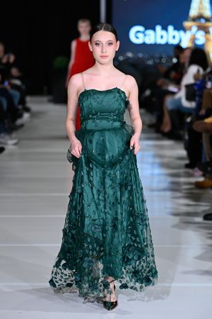 Model walks runway in emerald green textured dress with ruffled details at fashion show.