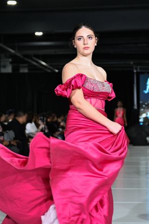 Model twirls in a vibrant hot pink ball gown with ruffle details on a sleek runway during fashion show.