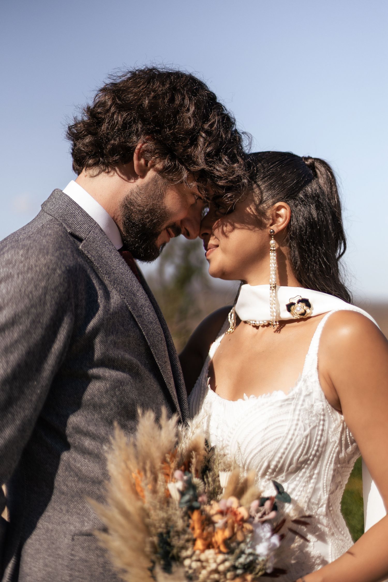 A romantic wedding couple shares an intimate moment in a field with dried pampas grass at sunset.