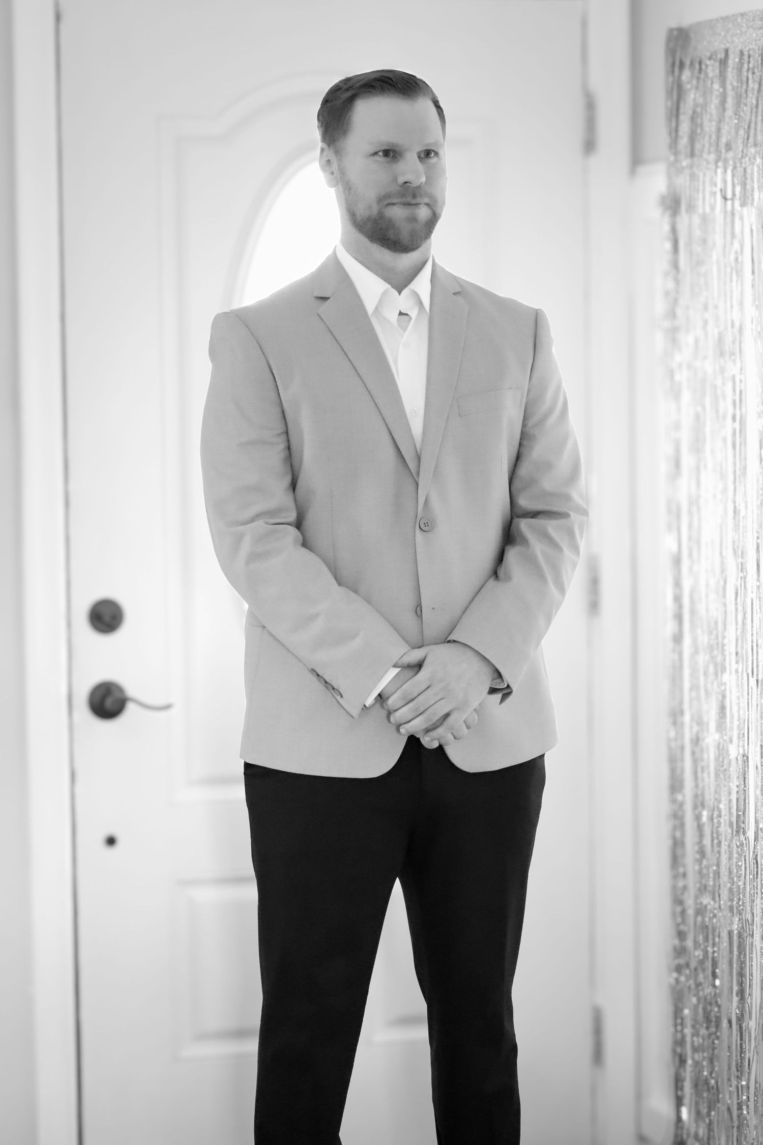 Professional portrait in a light gray suit jacket and dark pants against white door.