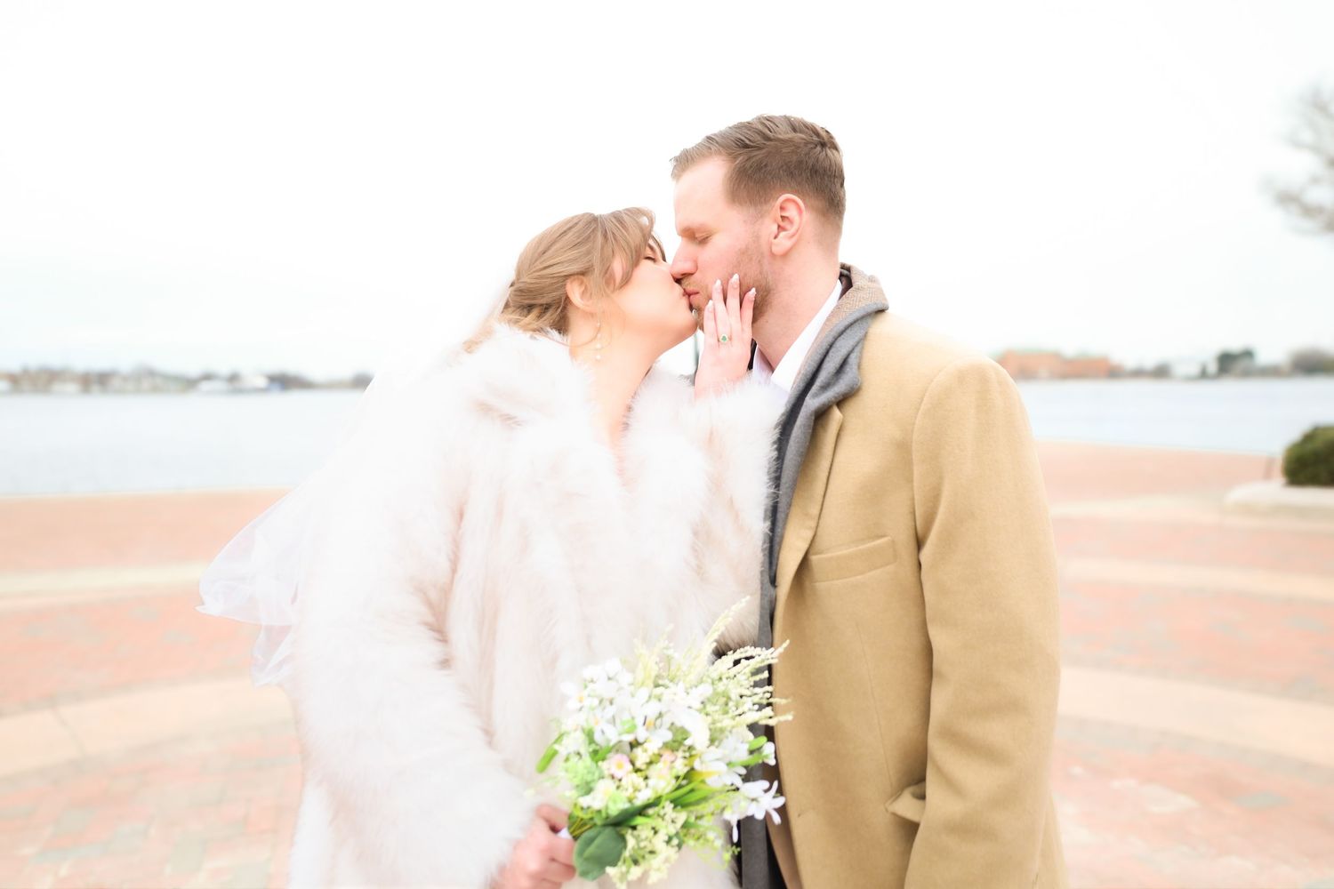 Romantic winter wedding moment with bouquet on waterfront brick path.