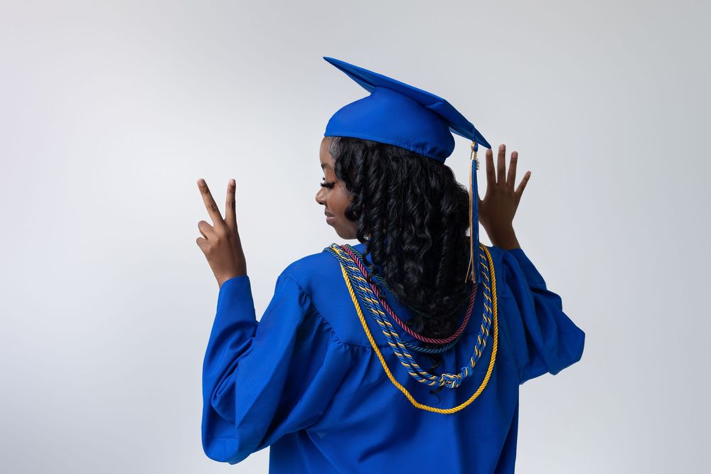 Graduate in royal blue cap and gown poses with peace signs while facing away from the camera.