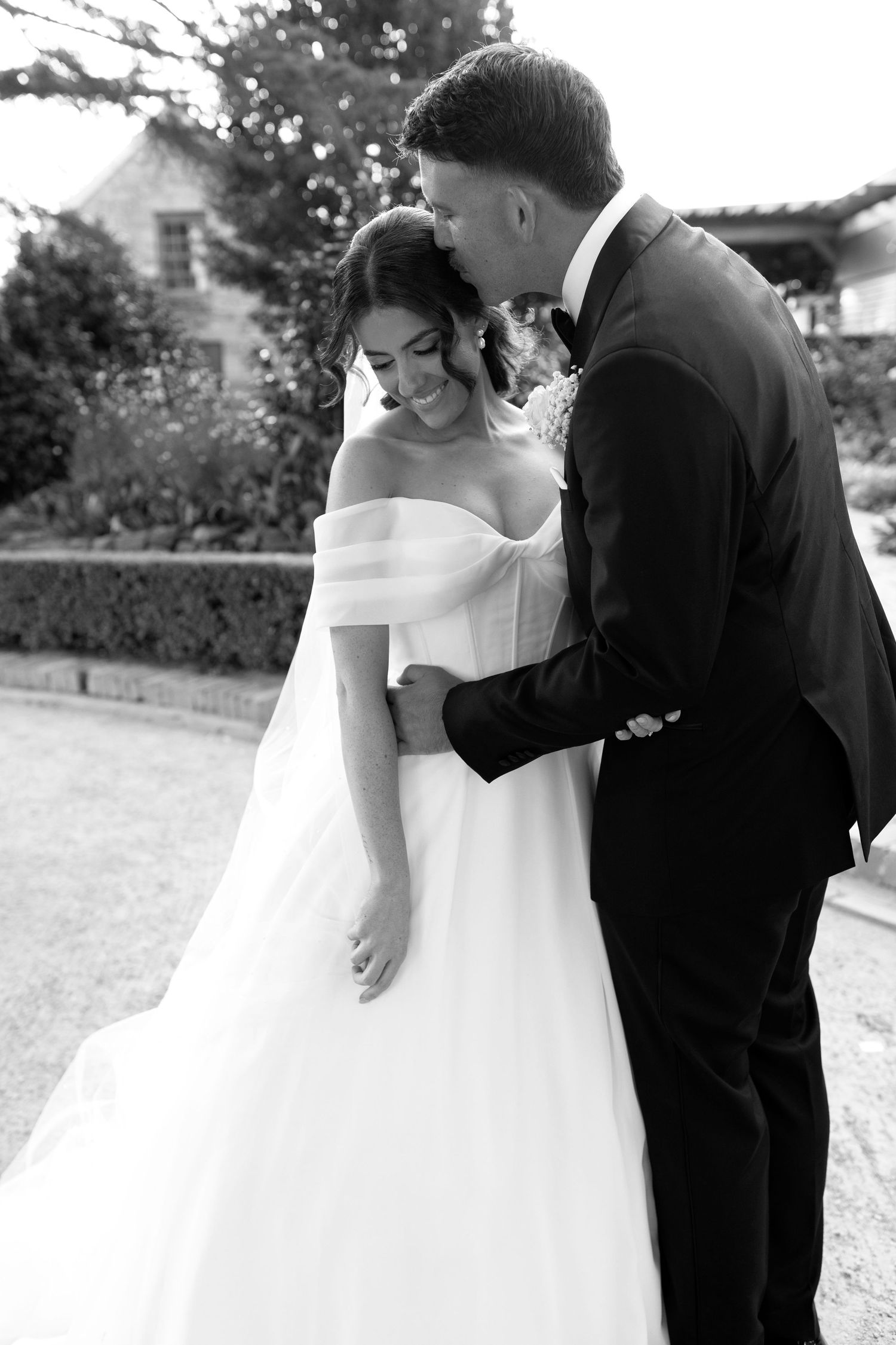 Couple in wedding attire walking away on a winding outdoor stone path as the bride's white dress flows in the wind.