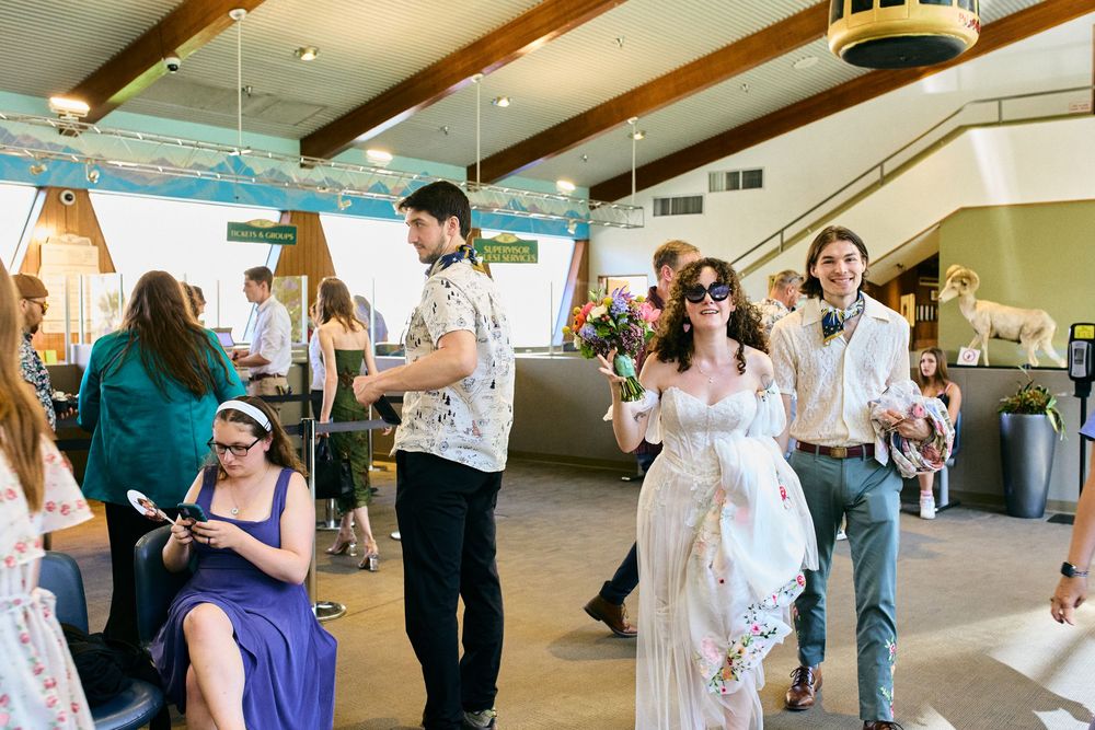 Wedding reception guests mingle and socialize in an elegant venue with exposed wooden beams and pendant lighting.