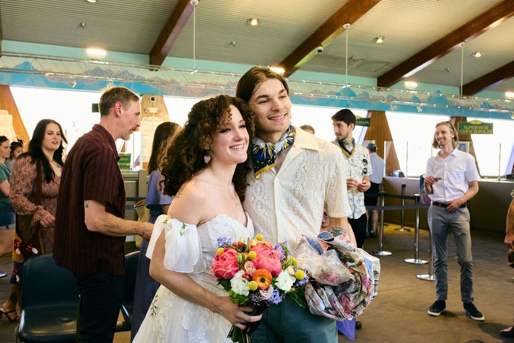 A couple shares a joyful moment together at an indoor reception while holding a vibrant bouquet of flowers.