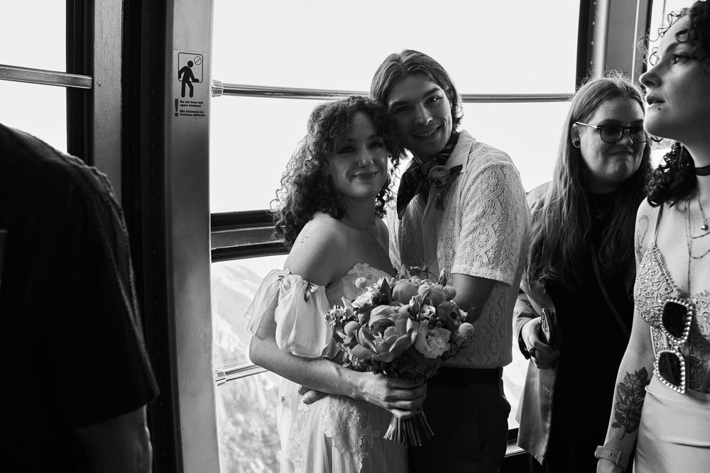 A black and white photograph shows a group of people gathered together by windows holding a bouquet of flowers.