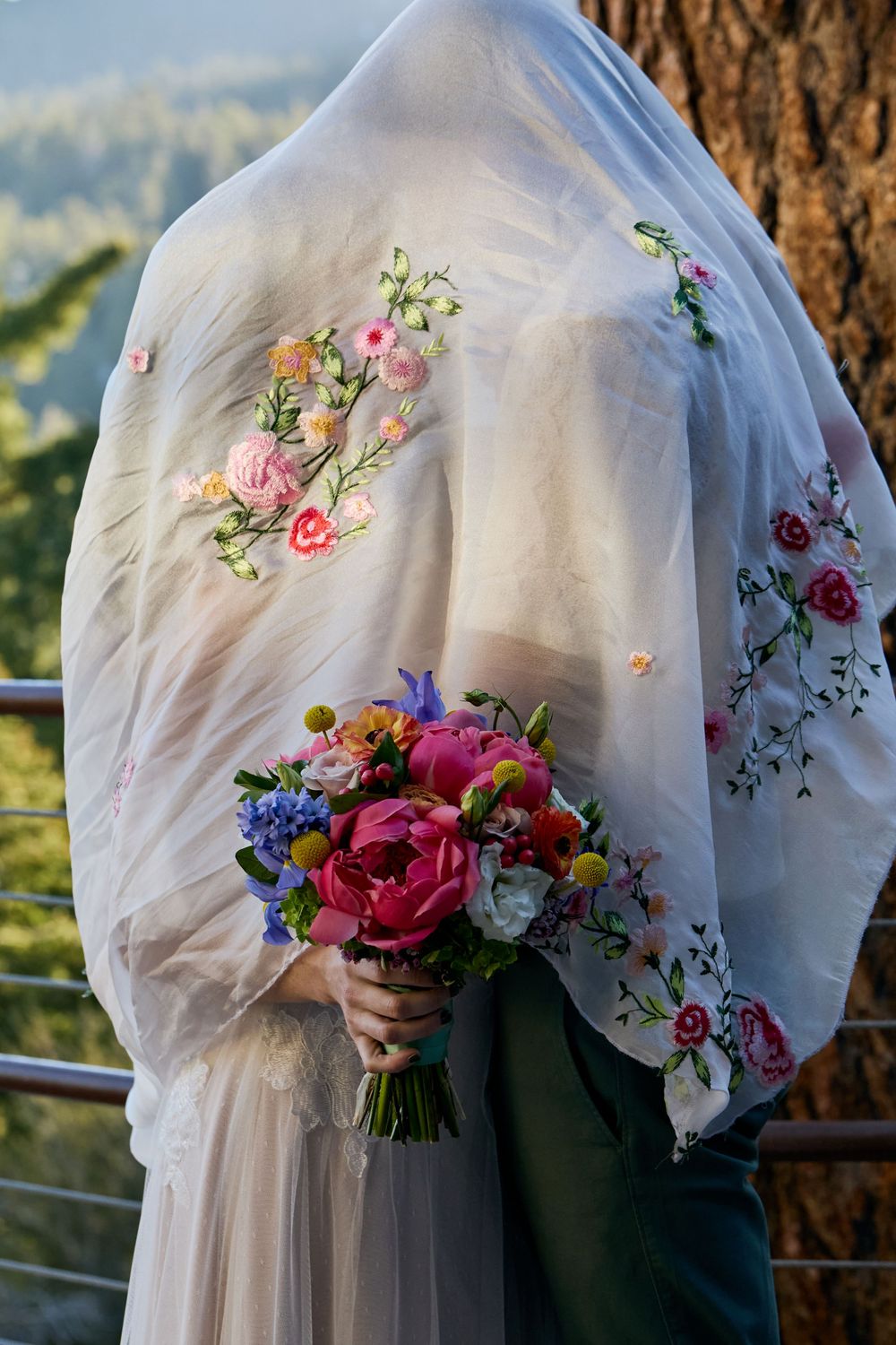 A bridal veil with delicate floral embroidery and a colorful bouquet of roses and wildflowers against a natural backdrop.