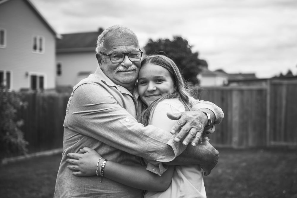 Black and white image of a grandfather hugging his granddaughter in the backyard.