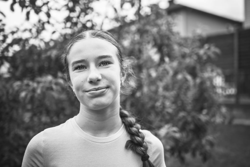 Black and white image of a young woman looking into the camera as she stands in front of an apple tree.