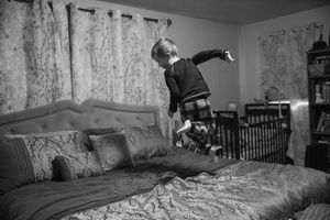 Child jumping on bed captured in dramatic black and white photography.