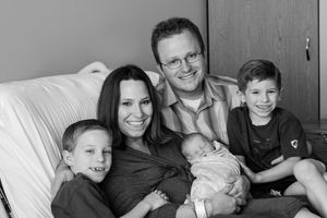 Family of five sitting together on white couch for casual portrait.