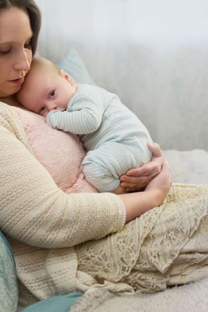 Mother in cream sweater holding sleeping baby wrapped in soft gray clothing.