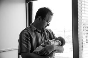 Parent holding newborn baby by window in black and white portrait.