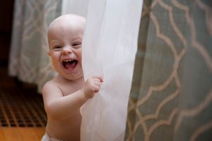 Joyful toddler laughing while playing peek-a-boo with sheer curtains.