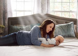 Mother and baby lying together on gray couch near window during lifestyle photoshoot.