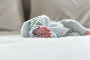 Close-up of infant wearing striped onesie resting on white bedding.