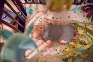 Baby sleeping peacefully on colorful patterned bedding with stuffed animals and toys.