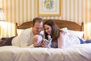 Family sharing an intimate moment together on a bed in a cozy bedroom with striped wallpaper.