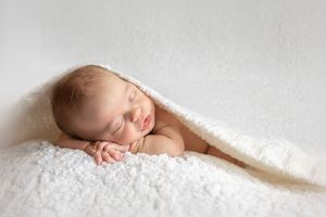 A sleeping baby lies peacefully on soft white bedding in a minimalist newborn photography style.