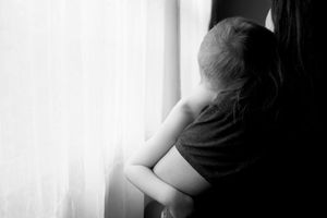 Silhouette of child looking out bright window in black and white.