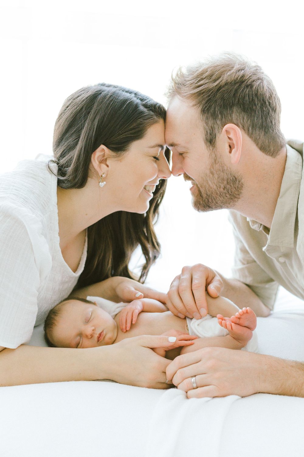 Parents sharing tender moment over their sleeping newborn in bright setting.