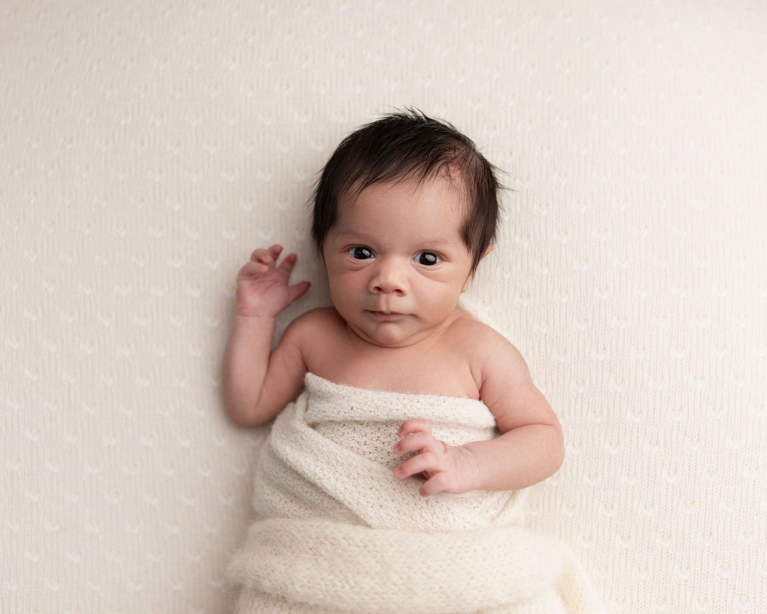 Awake newborn baby boy on the soft cream beanbag fabric.
