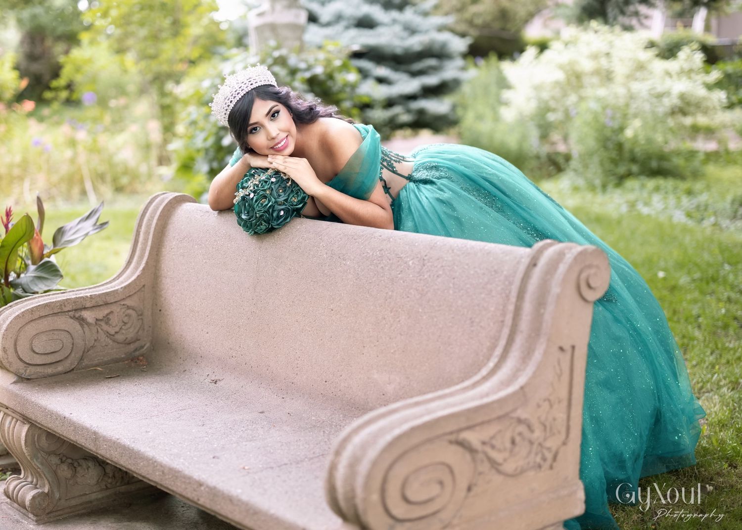 Vintage curved stone bench with ornate details stands in lush garden setting with turquoise accents.