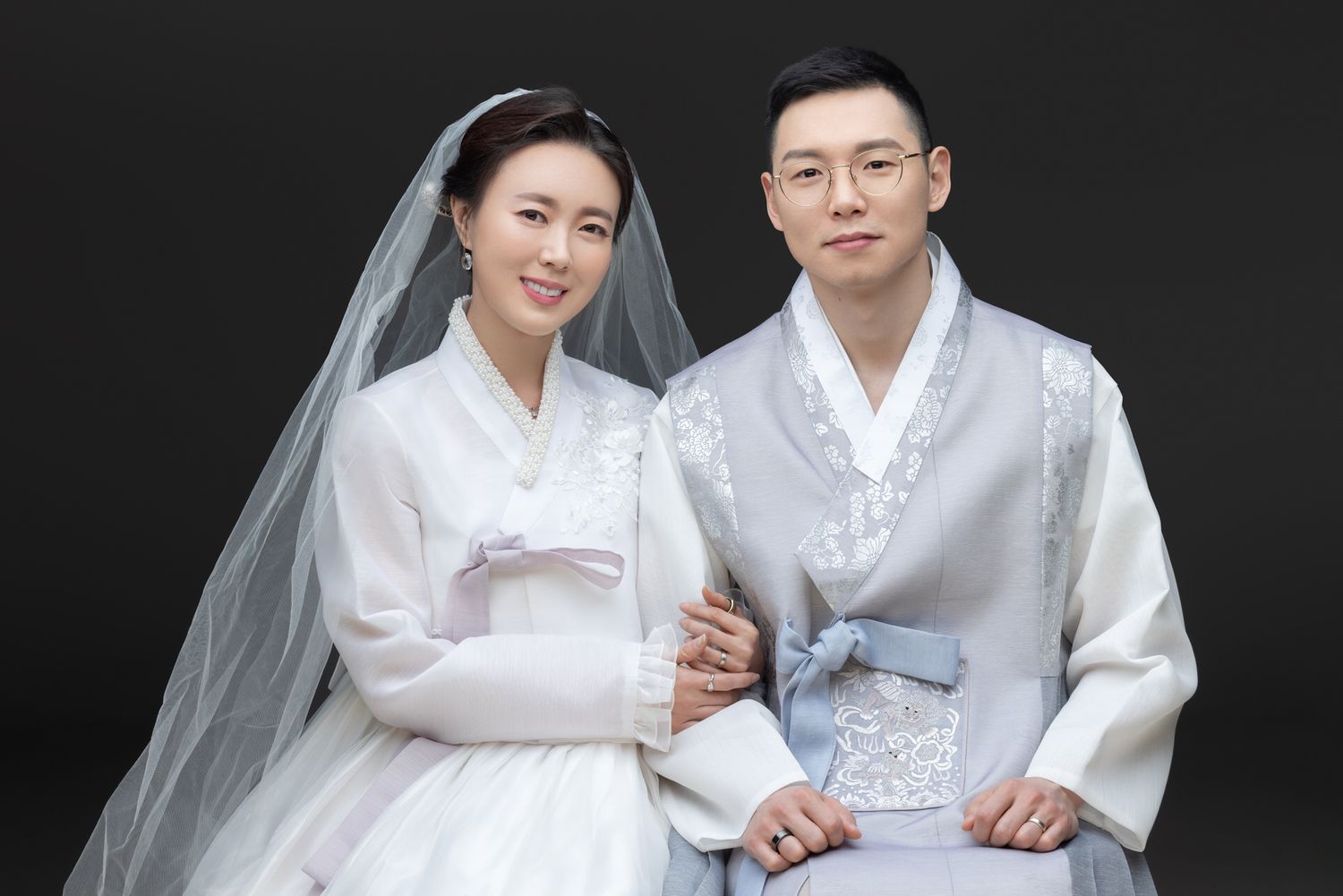 A couple wearing white traditional Korean hanbok outfits poses together in a series of wedding portraits.